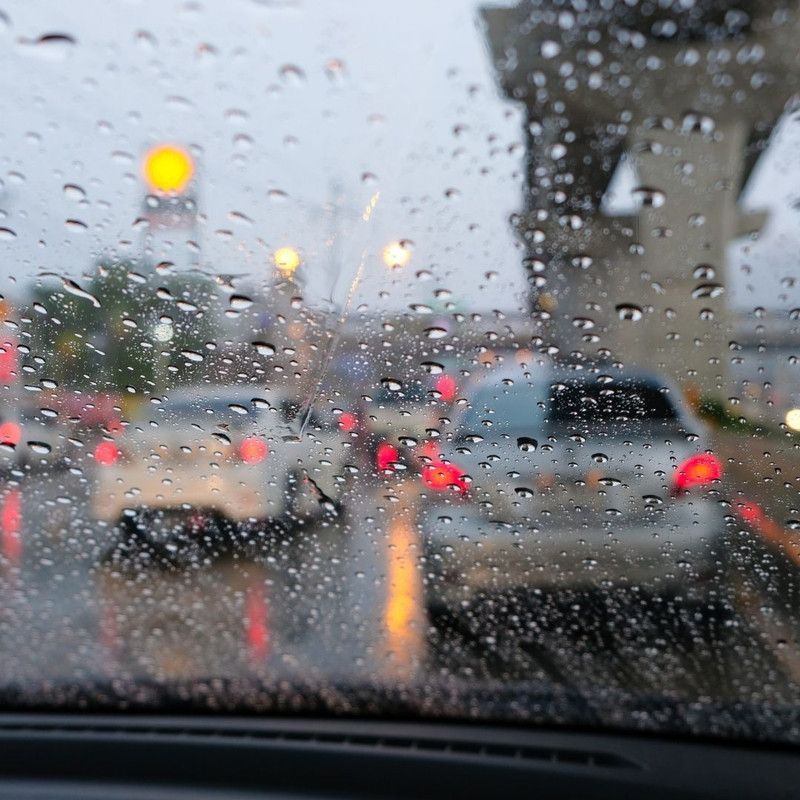 Rainy traffic scene; cars behind a windshield covered in raindrops.