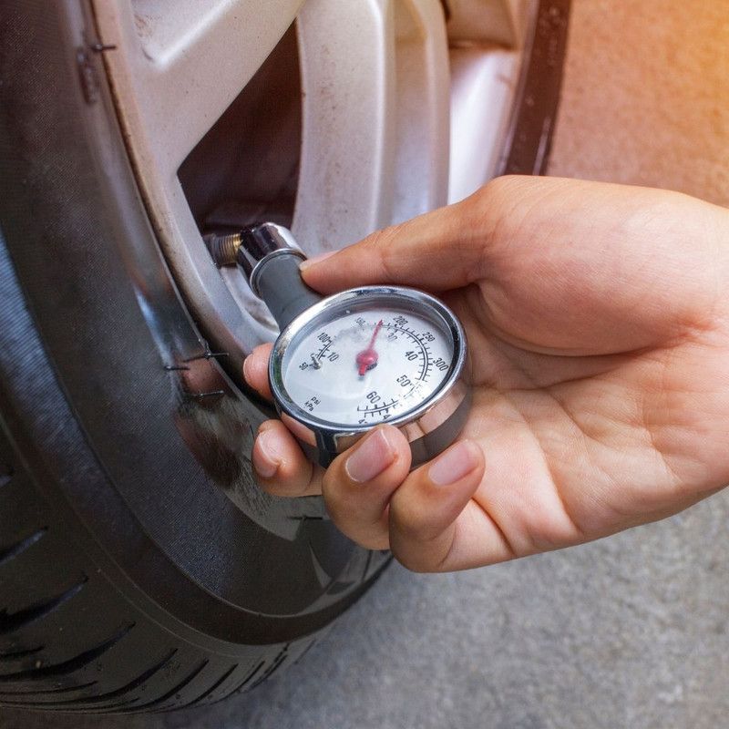 Hand checking tire pressure with a gauge next to a car tire.