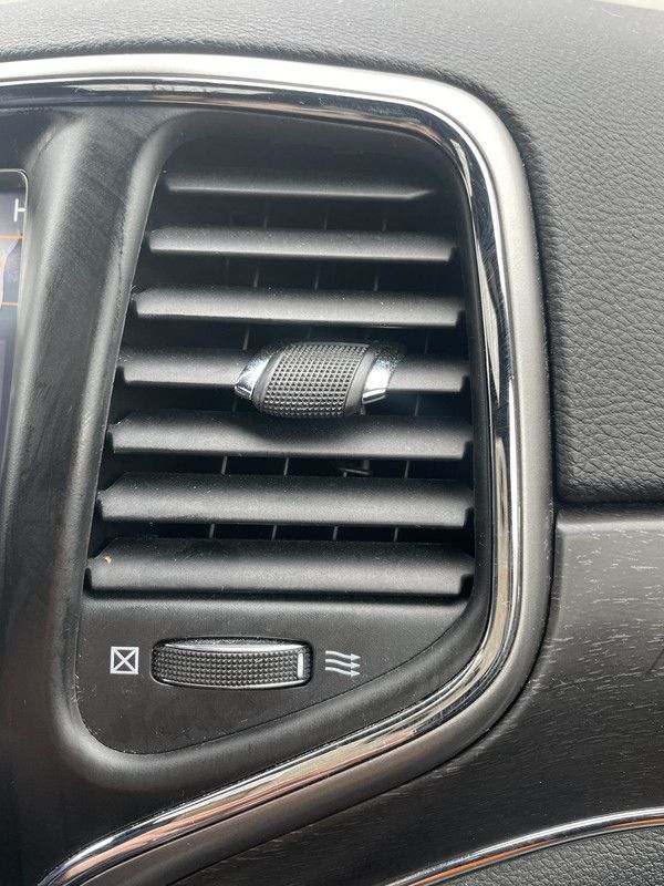 Close-up of car air vent with adjustable louvers, surrounded by a chrome frame, and temperature control below.