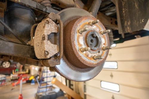 Rusty car brake rotor and caliper, viewed from beneath the vehicle.