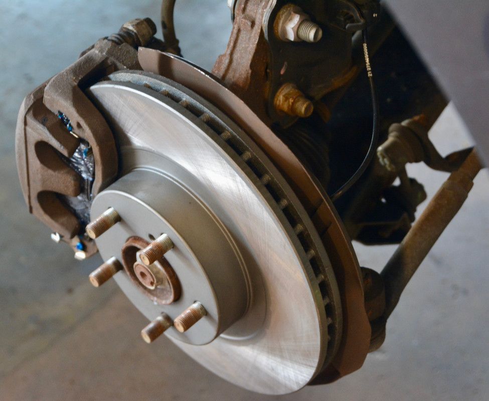 Car brake assembly with rotor, caliper, and lug nuts, showing rust and metal.