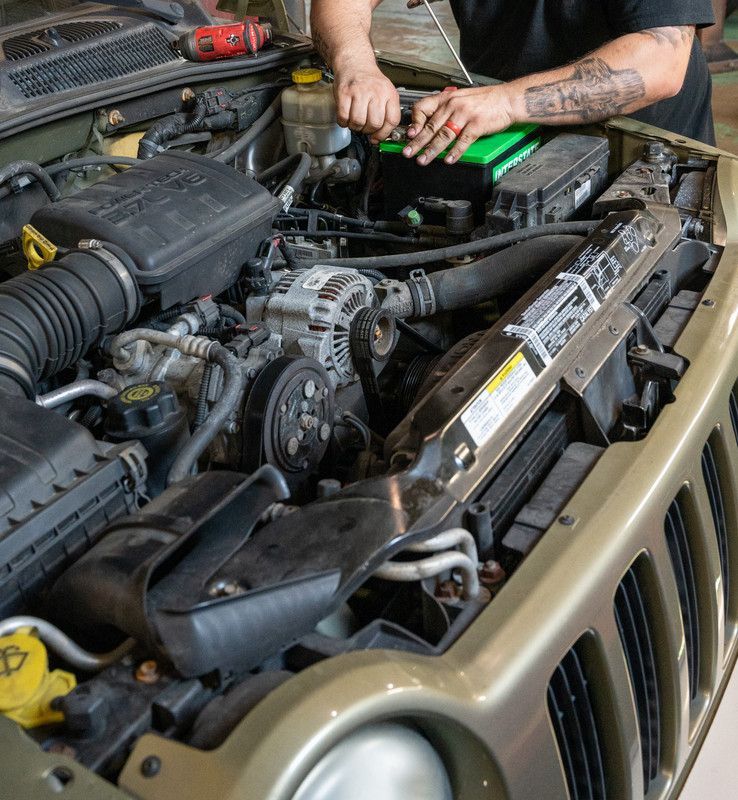 Mechanic working on a car engine bay, focused on the battery replacement, green car, tools visible.
