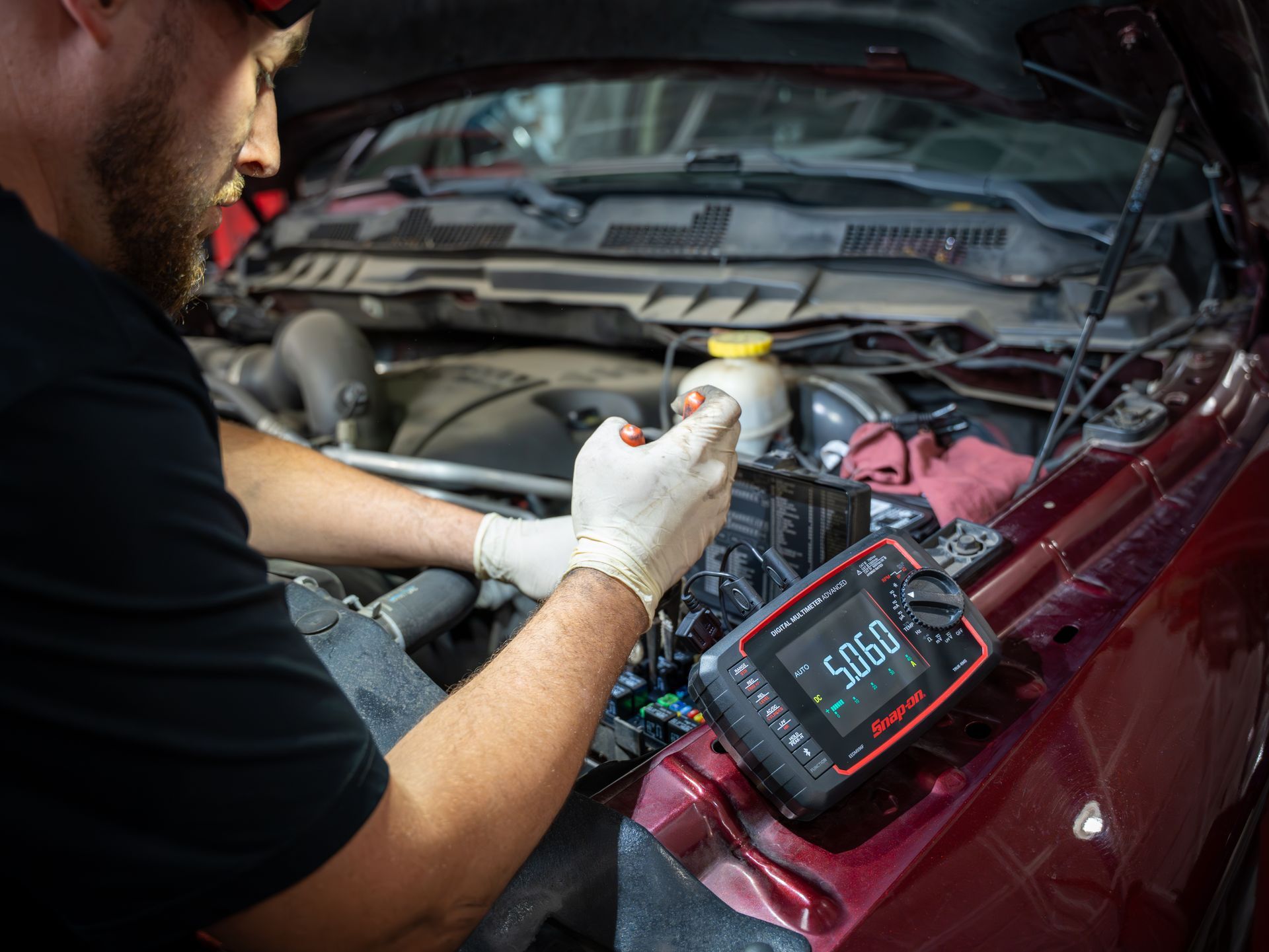 Mechanic testing a car battery with a digital multimeter under the hood .