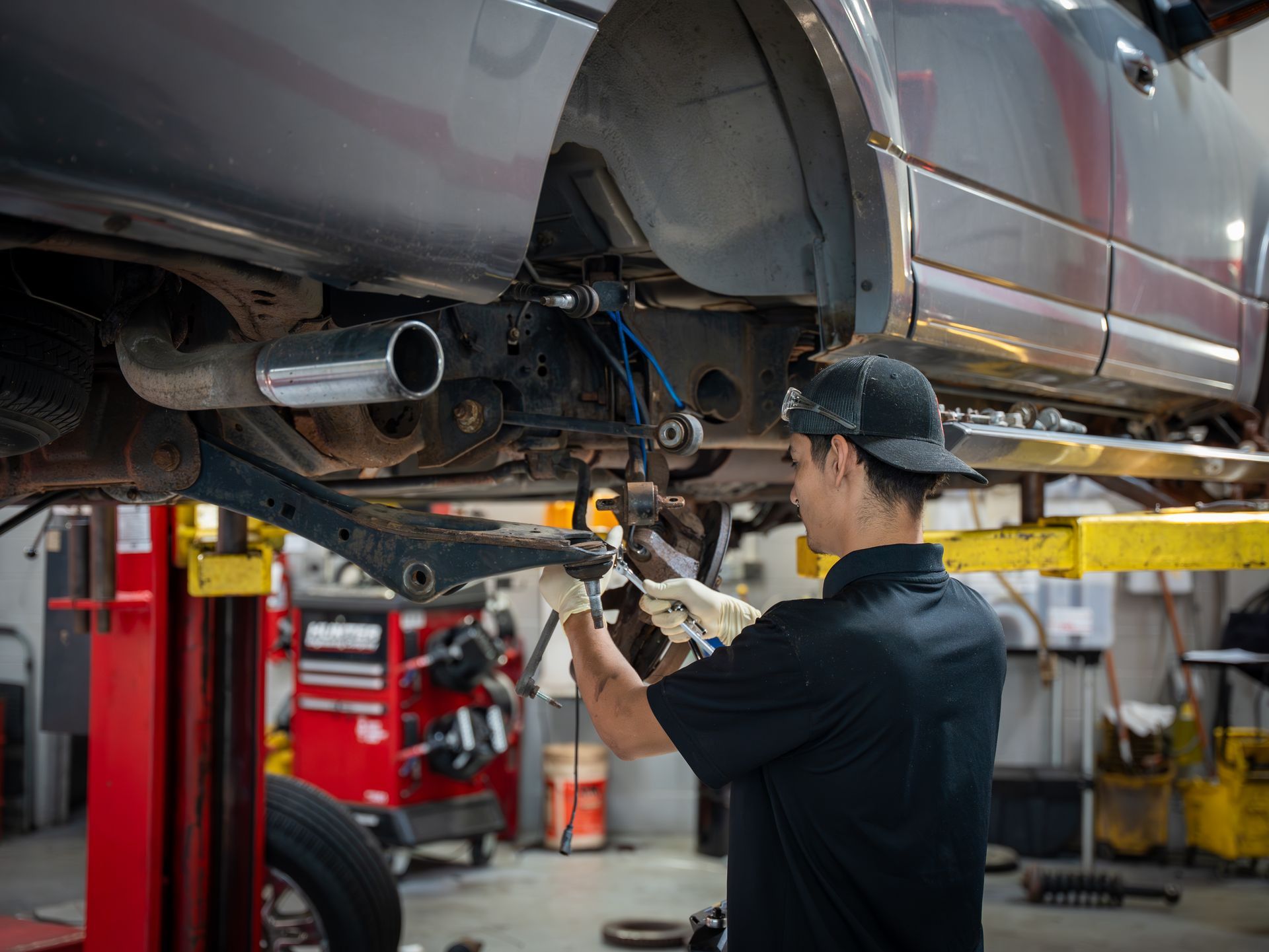Technician inspecting and repairing suspension components on a vehicle lifted in an auto repair shop