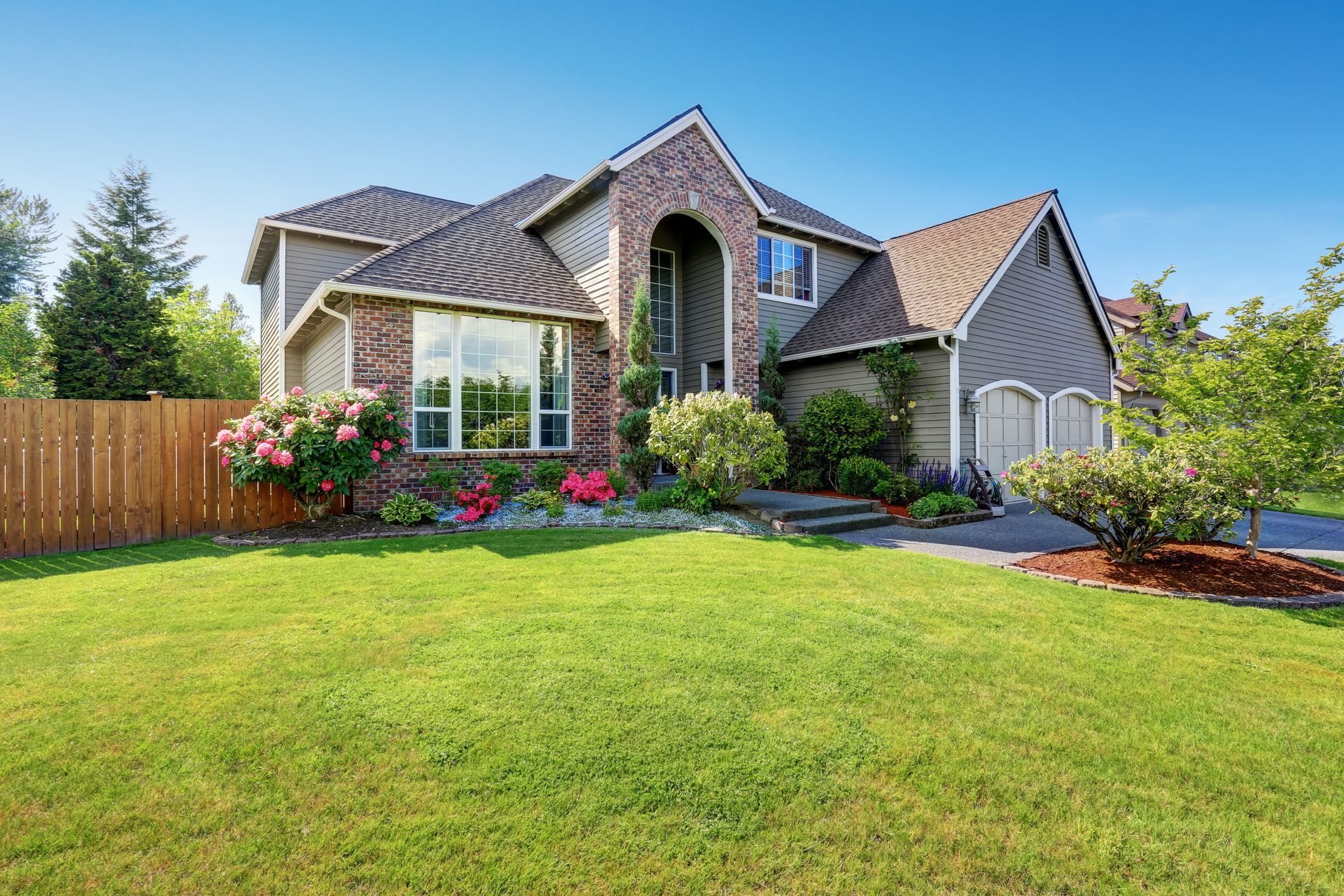 Large house with brick and gray siding, green lawn, blue sky.
