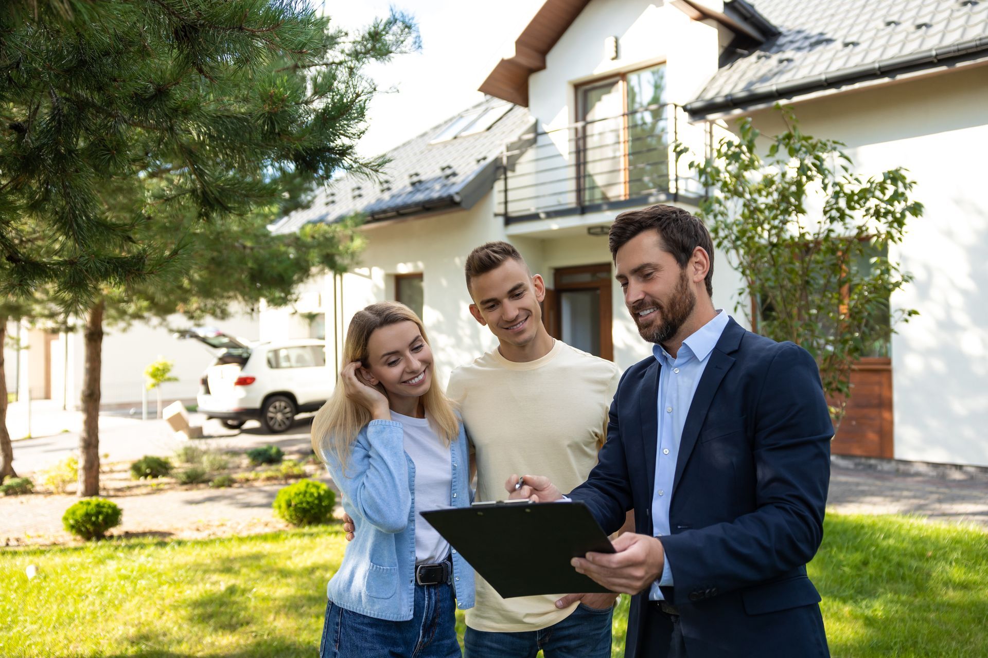 Real estate agent showing paperwork to a couple in front of a house.