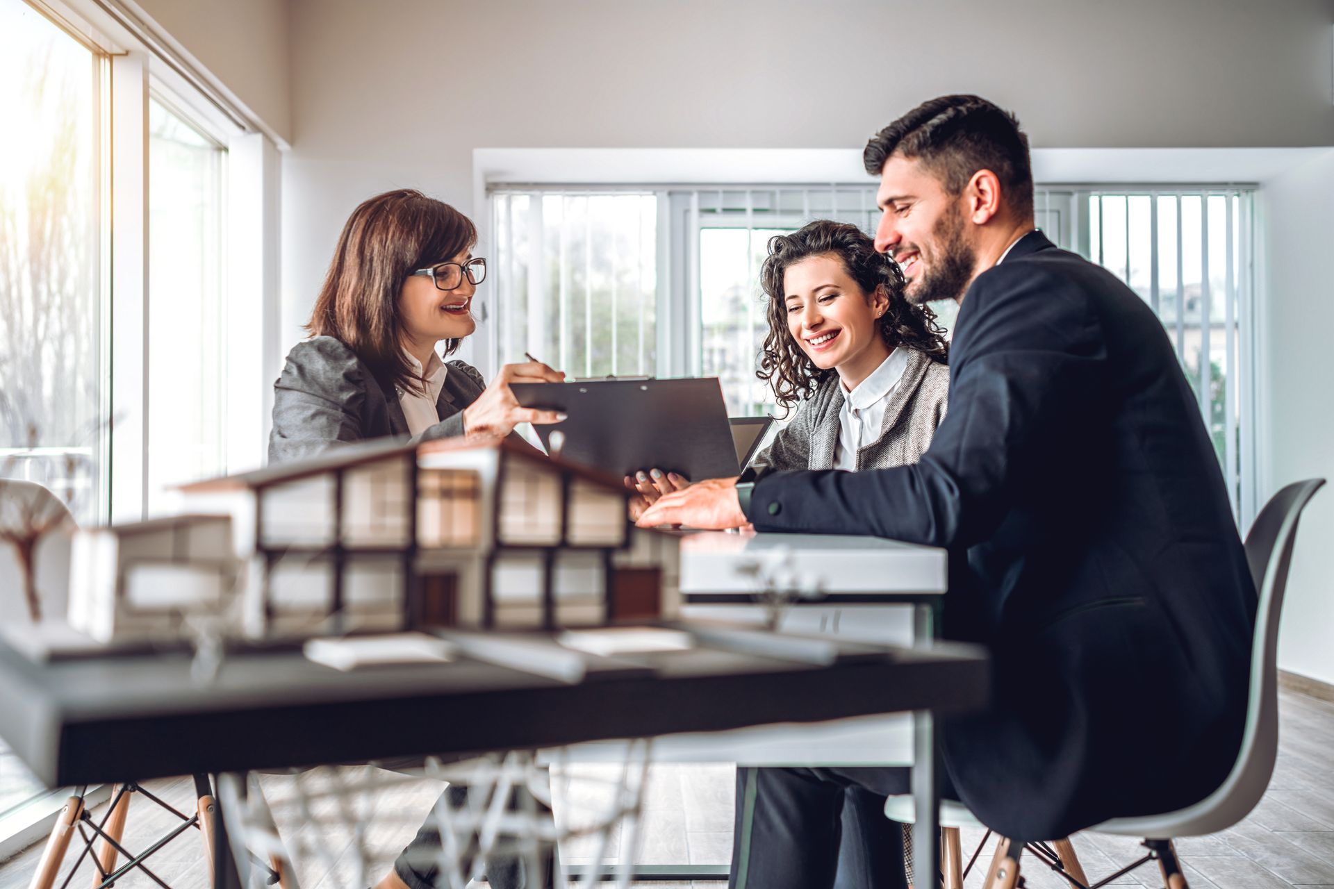 Real estate agent with couple reviewing documents, discussing house model at a table.