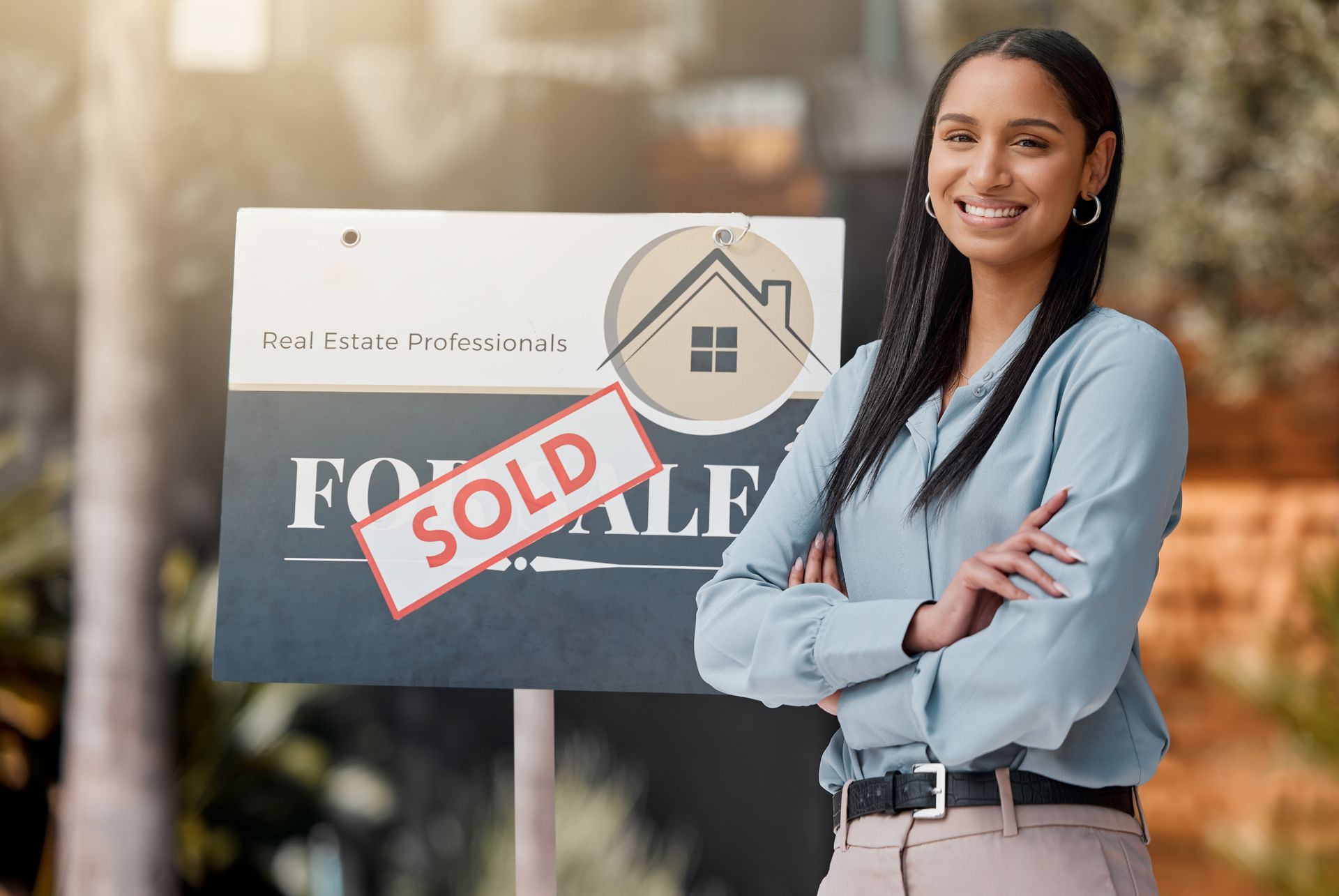 Real estate agent standing confidently in front of a “sold” sign, smiling.