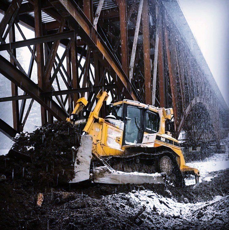 A bulldozer is working under a bridge in the snow