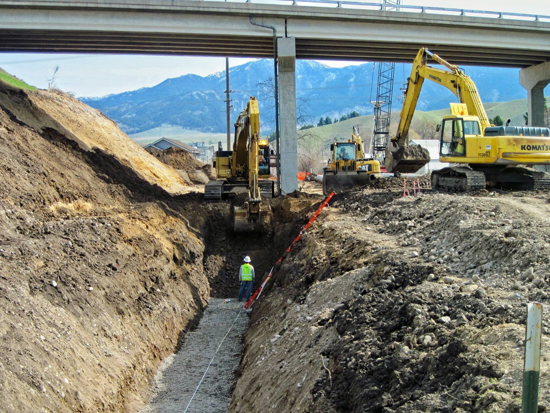 Construction workers are digging a trench under a bridge