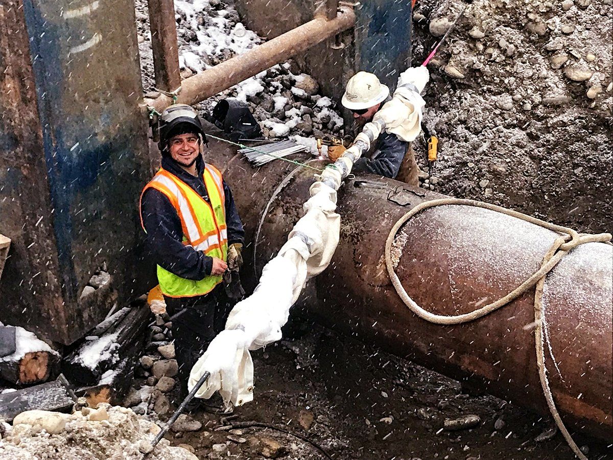 A man in a yellow vest is standing next to a large pipe.