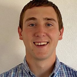 A young man in a plaid shirt is smiling for the camera.