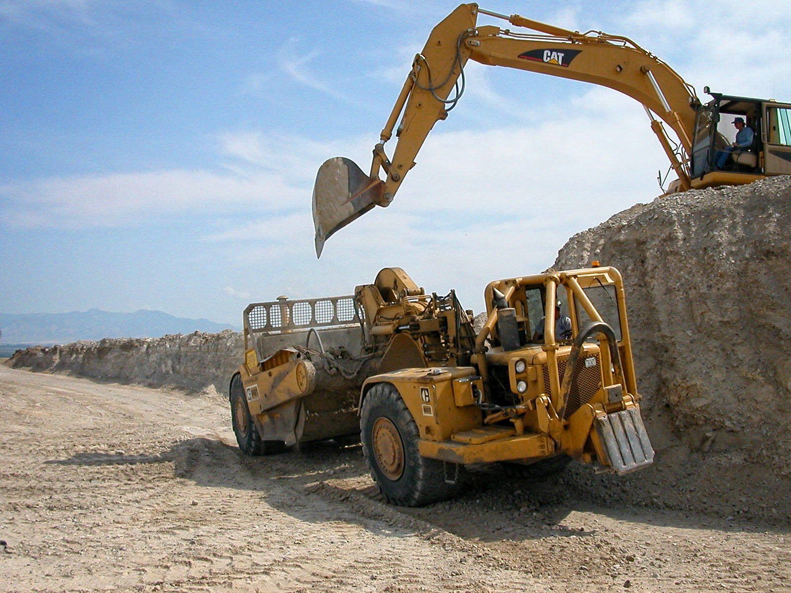 A cat excavator is loading dirt into a dump truck