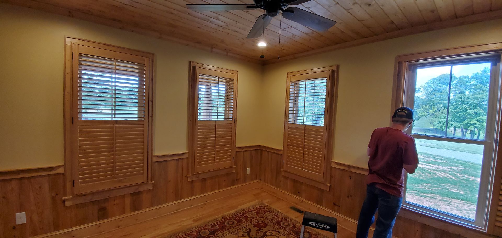 Wood-paneled room with windows and a person standing by a large window, looking outside.