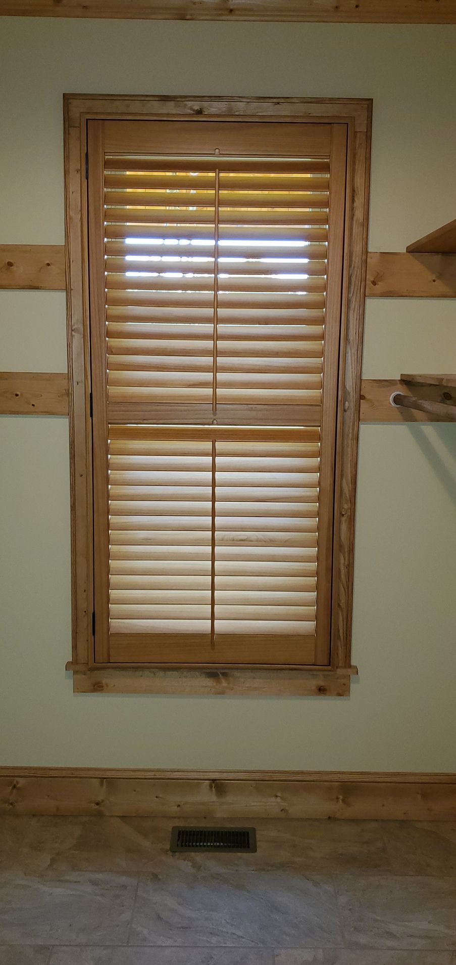Wooden blind-covered window set in a white wall with wood trim and shelf brackets on either side.