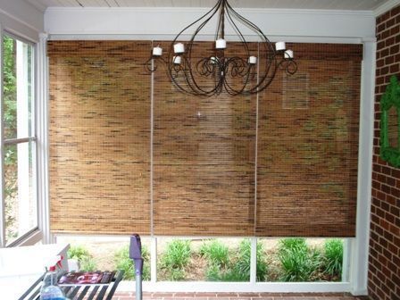 Bamboo shades covering a bright window, with a wrought-iron chandelier hanging overhead.