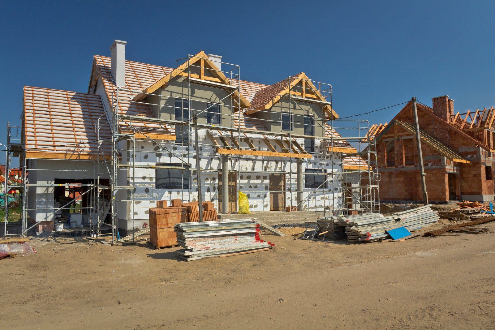 Houses under construction with scaffolding, surrounded by building materials, under a clear blue sky.