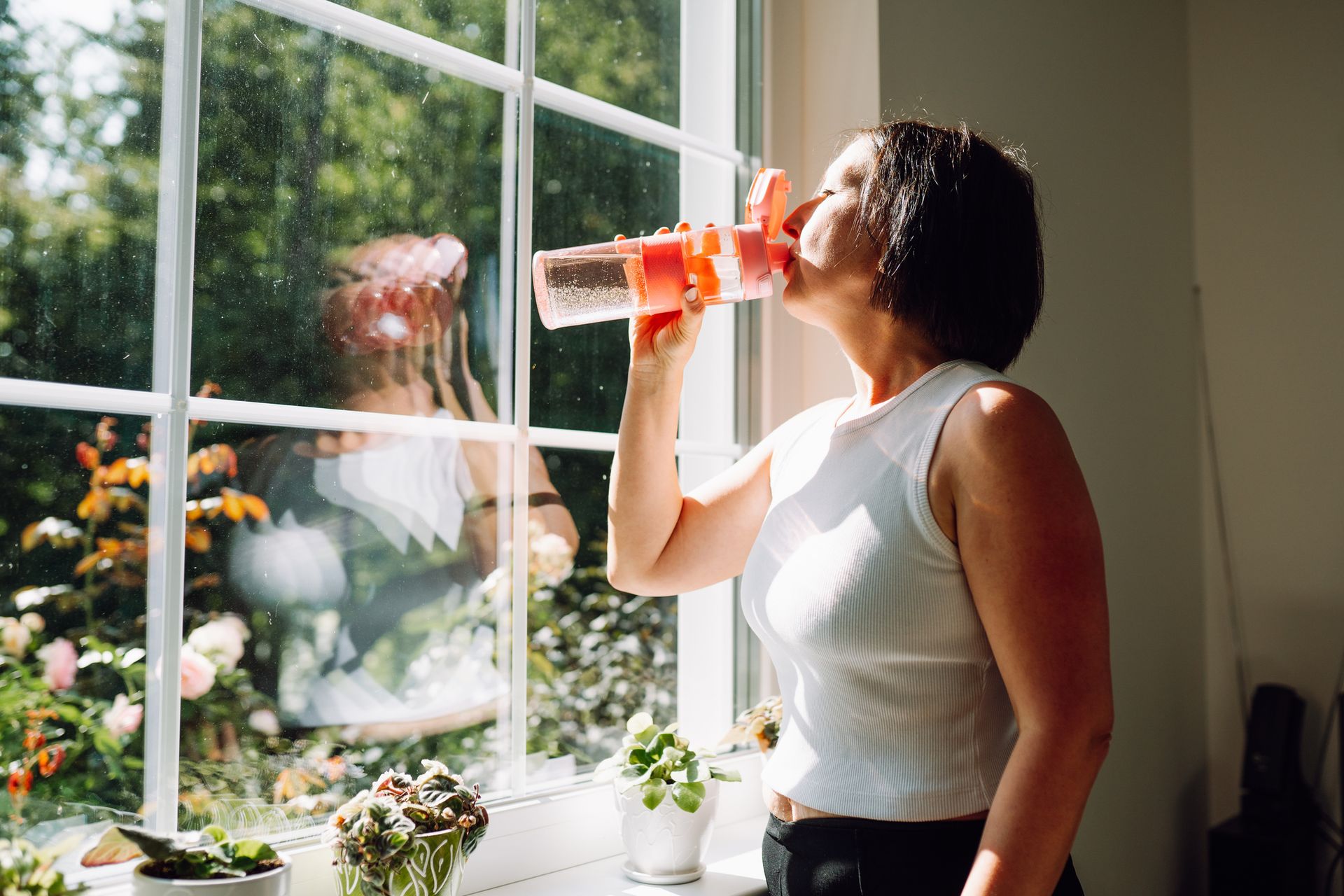 Woman in sportswear drink water after home exercising.