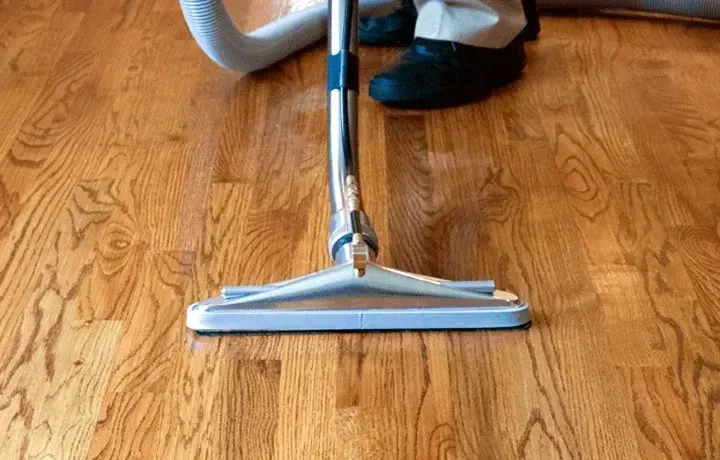 A person is vacuuming a wooden floor with a vacuum cleaner.