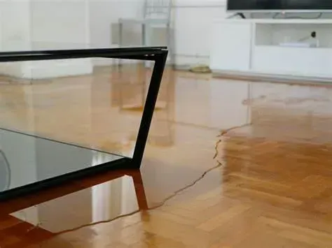 A glass coffee table is sitting on a wooden floor in a living room.