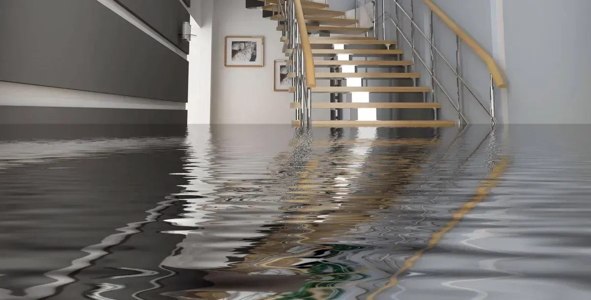 A flooded hallway with stairs and water on the floor.