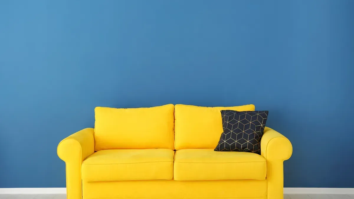 A yellow couch is sitting in front of a blue wall.