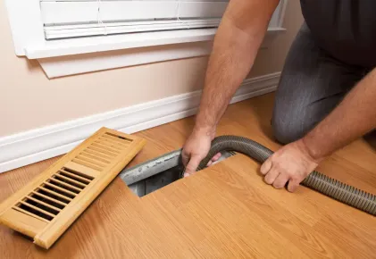 A man is using a vacuum cleaner to clean a vent on the floor.