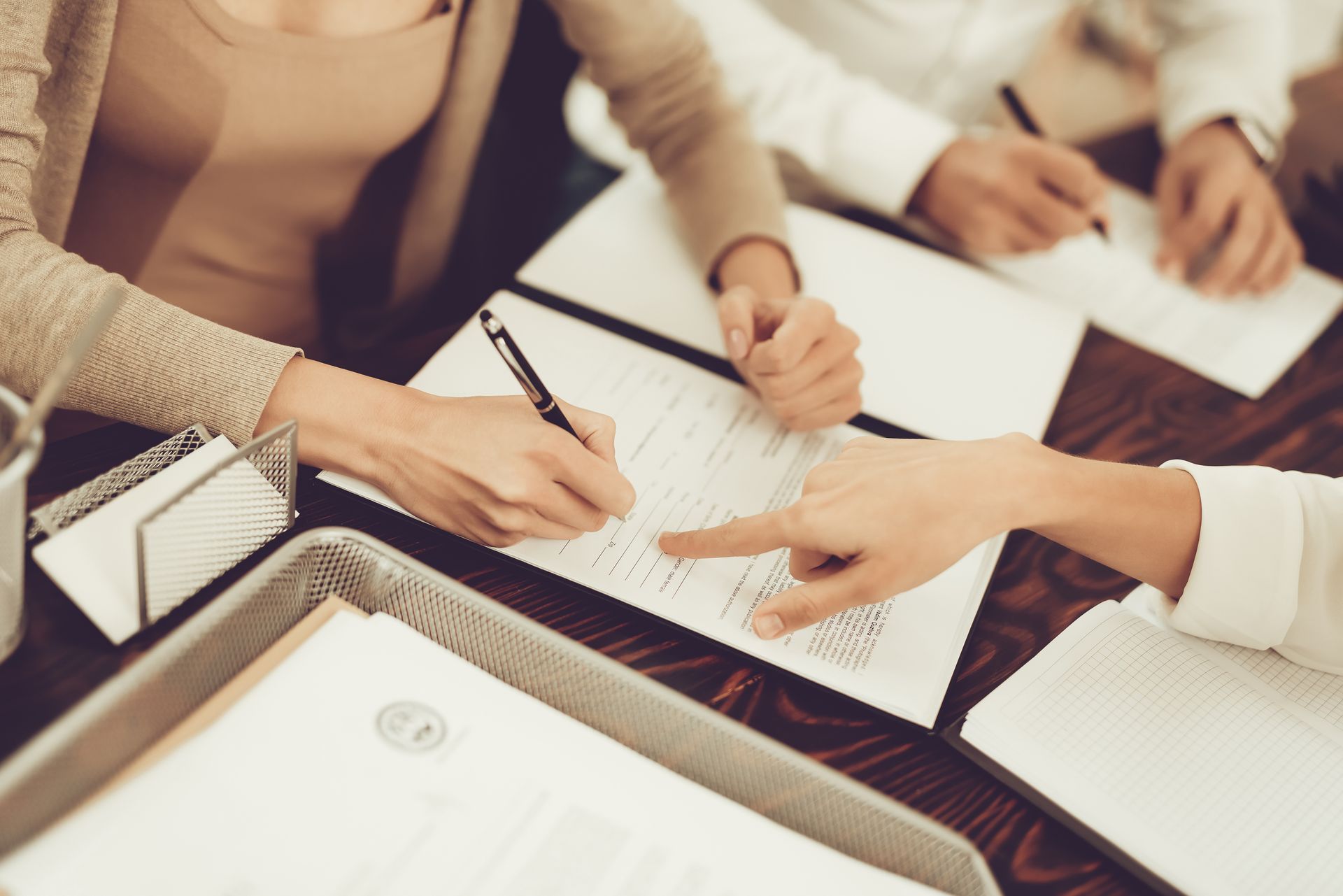 Hands signing documents at a table. One person points, while another writes with a pen.