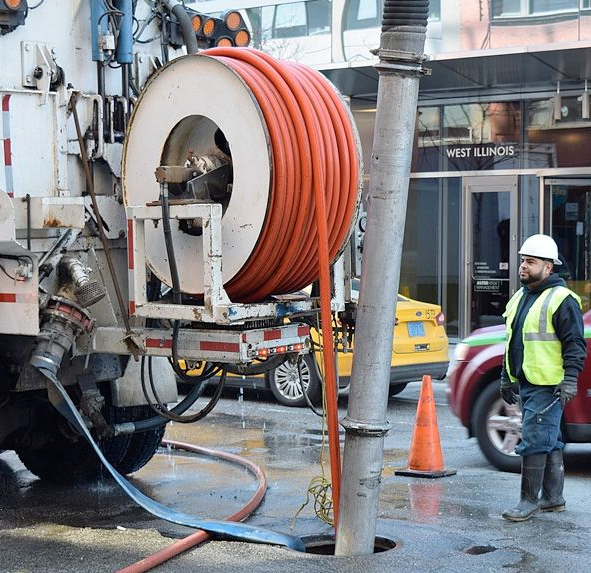 Capre all'interno di una stalla con pavimento ricoperto di fieno e recinzione metallica. Una luce intensa filtra dal retro.