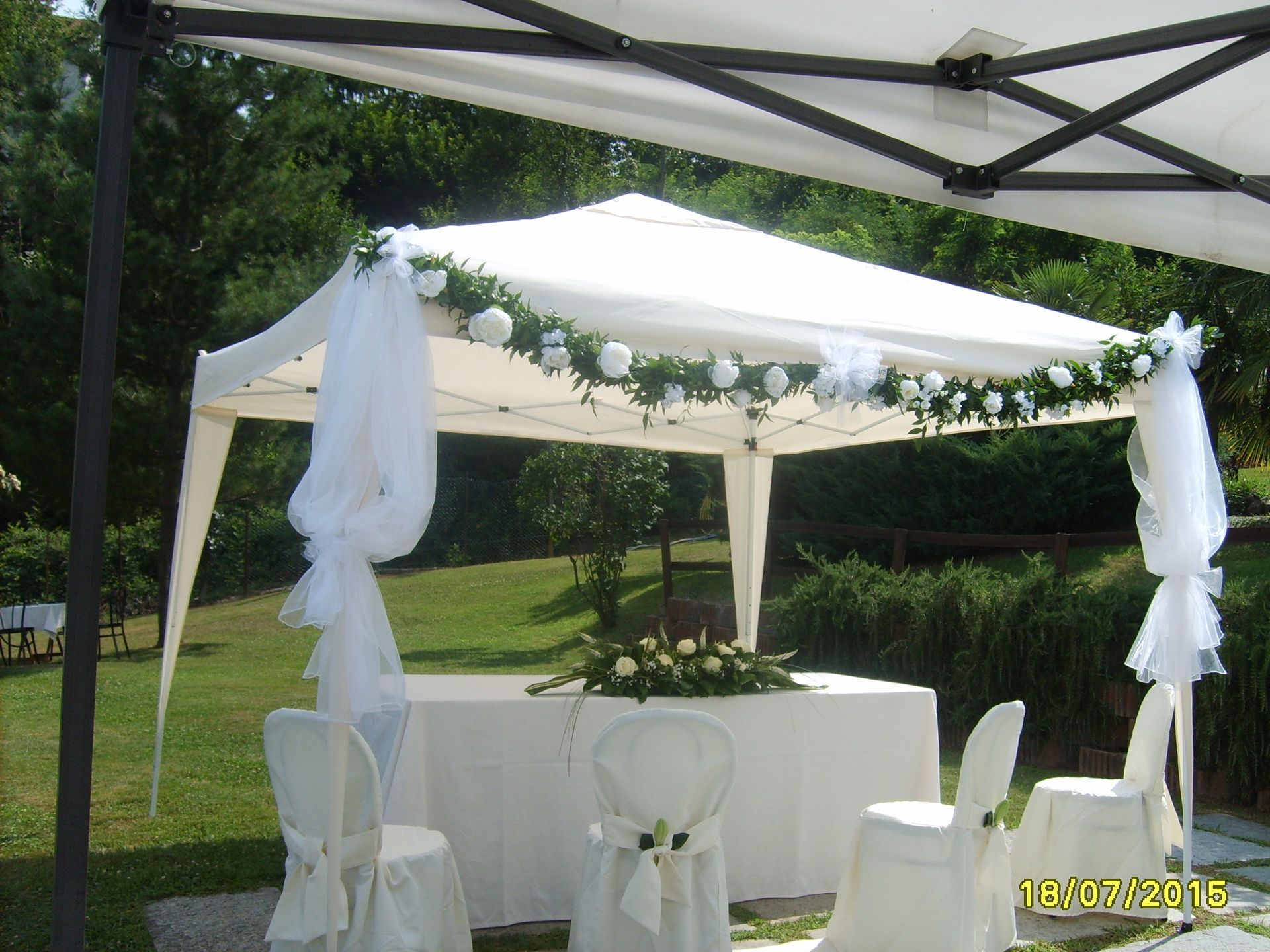Allestimento per la cerimonia nuziale con baldacchino bianco, tessuto drappeggiato, decorazioni floreali e sedie.