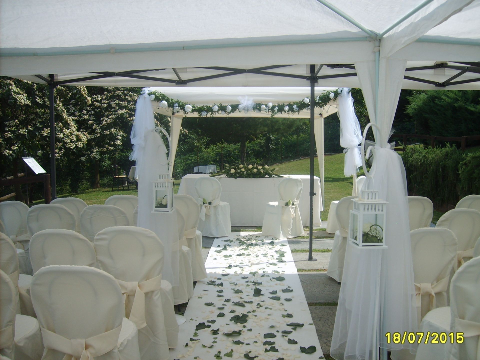 Allestimento per cerimonia nuziale all'aperto con sedie bianche, navata centrale, altare sotto un gazebo.