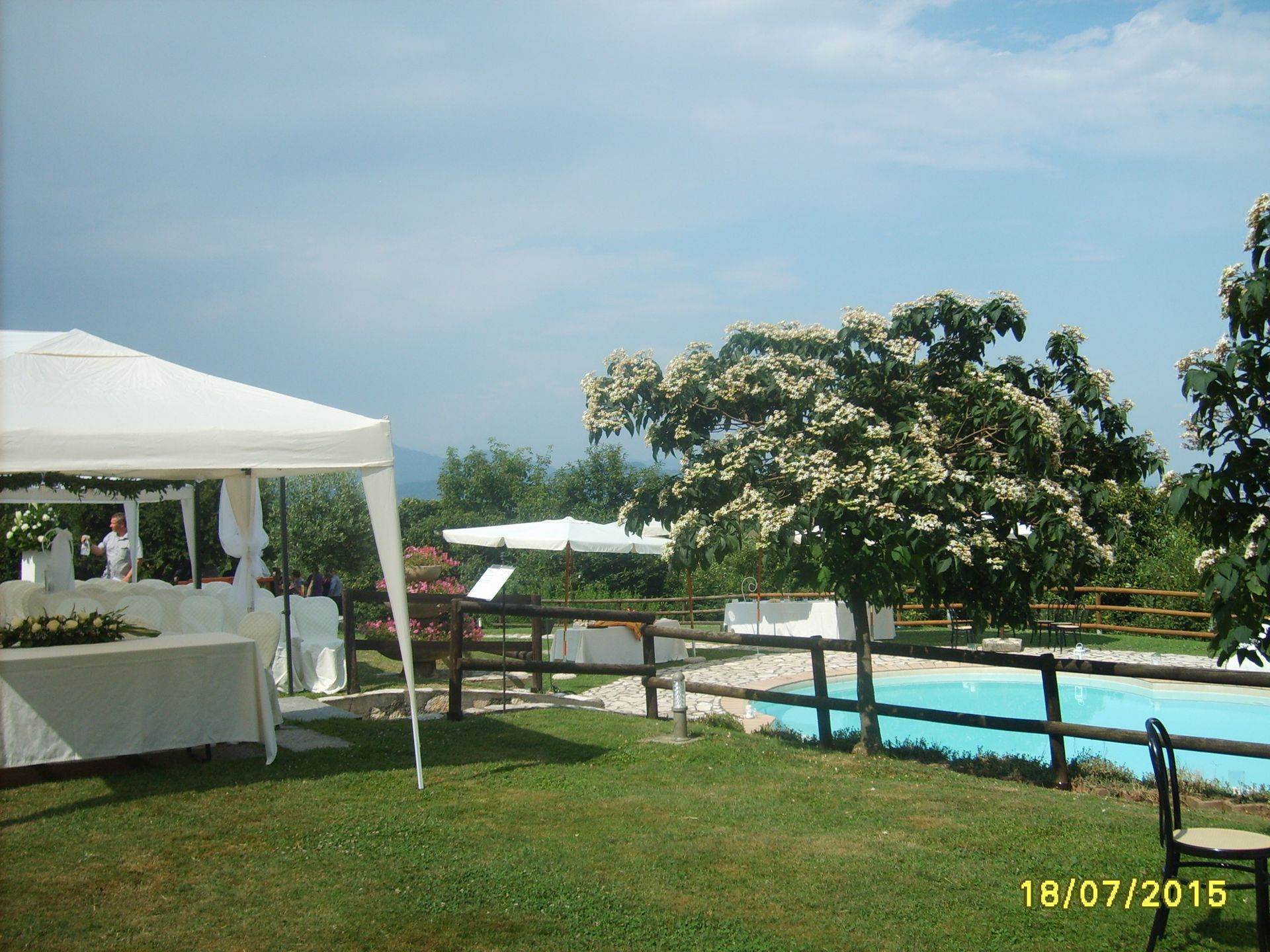 Spazio per eventi all'aperto con piscina, gazebo e prato sotto un cielo azzurro.