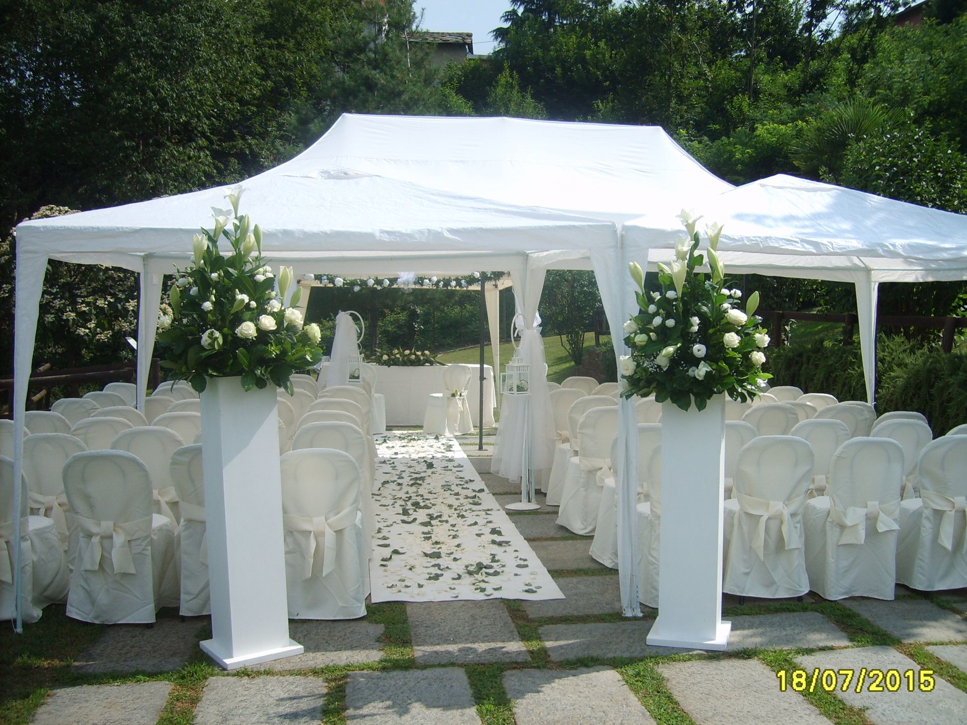 La cerimonia nuziale si è svolta sotto una tenda bianca; file di sedie si affacciano su una navata con composizioni floreali.