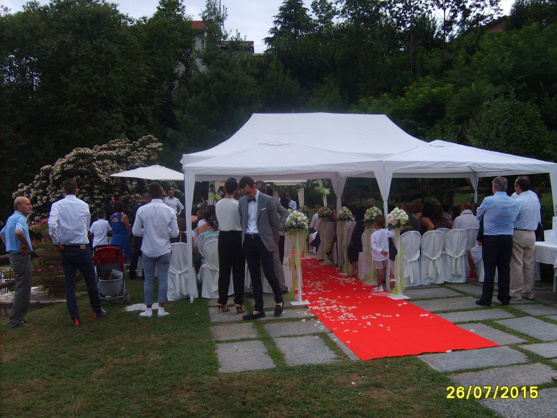 Cerimonia nuziale sotto una tenda bianca, tappeto rosso, invitati sul prato.