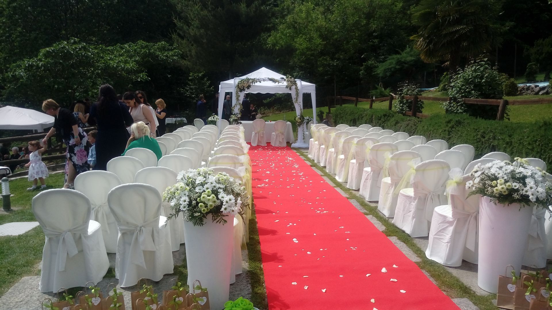 Allestimento per la cerimonia nuziale con sedie bianche, tappeto rosso e decorazioni floreali all'aperto.