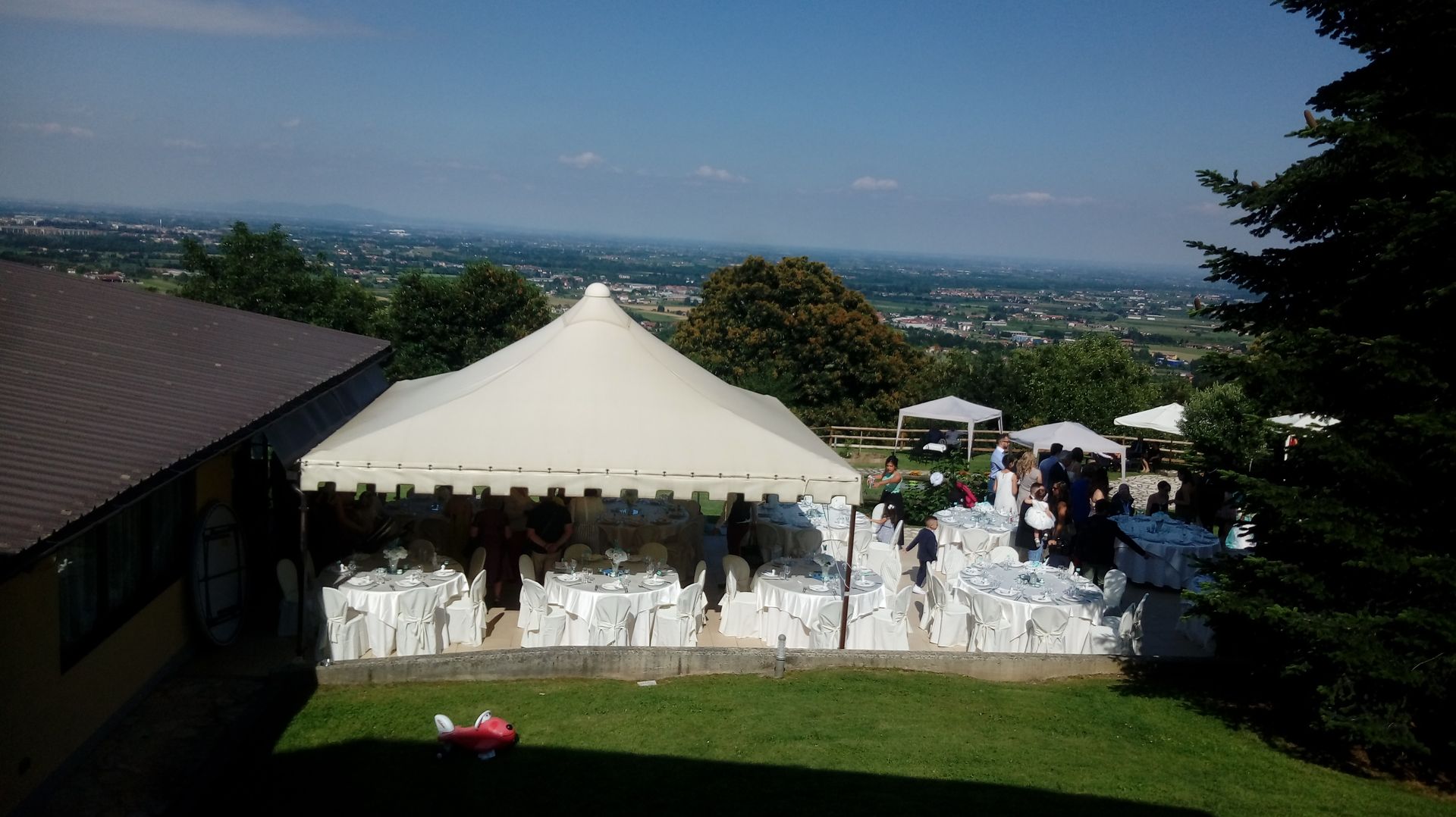 Evento all'aperto con tende bianche, tavoli e sedie sulla cima di una collina che domina la città.