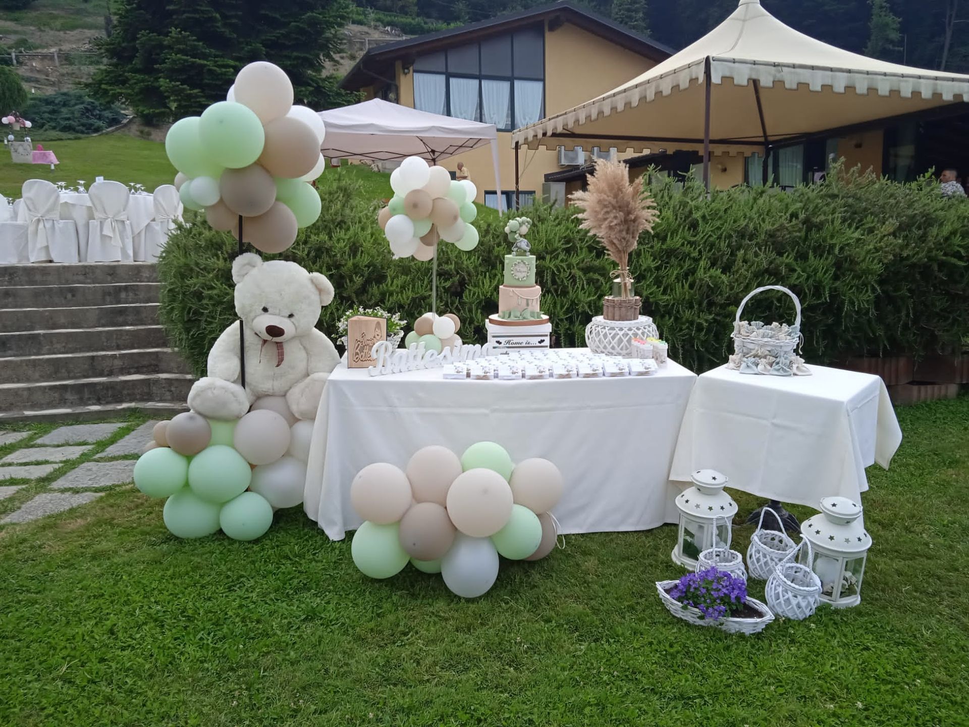 Festa all'aperto con orsacchiotto, palloncini, torta e decorazioni su un prato erboso.