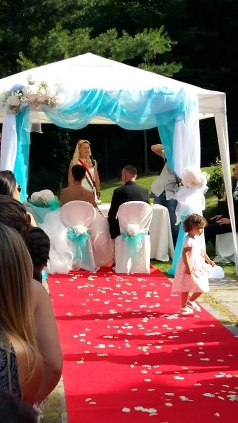 Cerimonia nuziale con gli sposi sotto un gazebo decorato, tappeto rosso e petali di fiori.