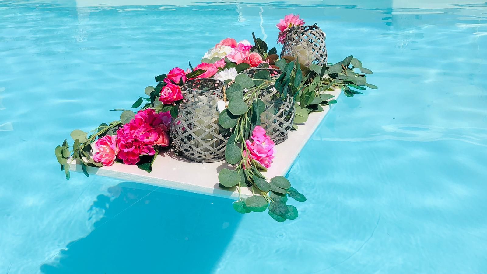 Composizione floreale galleggiante in una piscina, con fiori rosa, verde e portacandele decorativi.