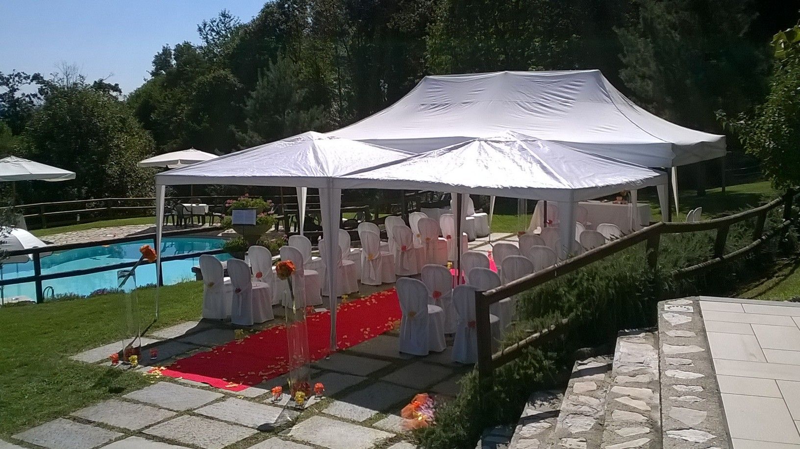 Allestimento per la cerimonia nuziale con tende bianche, tappeto rosso, sedie e piscina sullo sfondo.