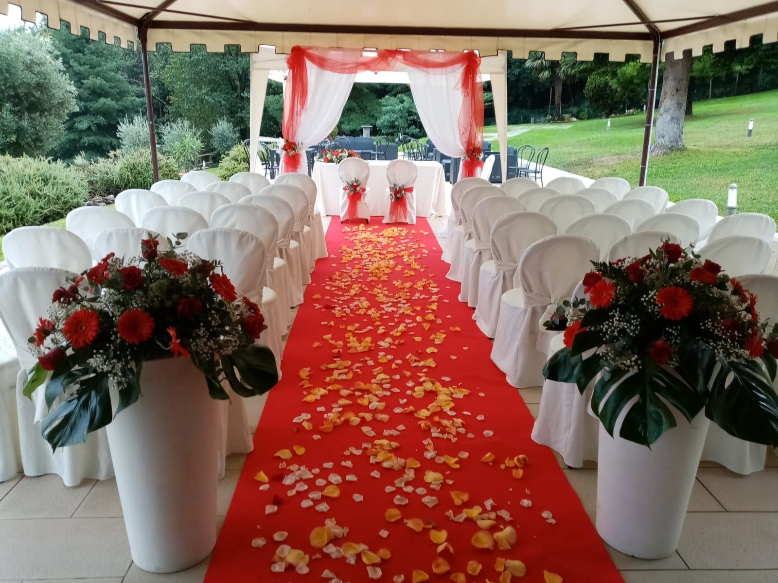 Allestimento per la cerimonia nuziale con tappeto rosso, sedie bianche e composizioni floreali.