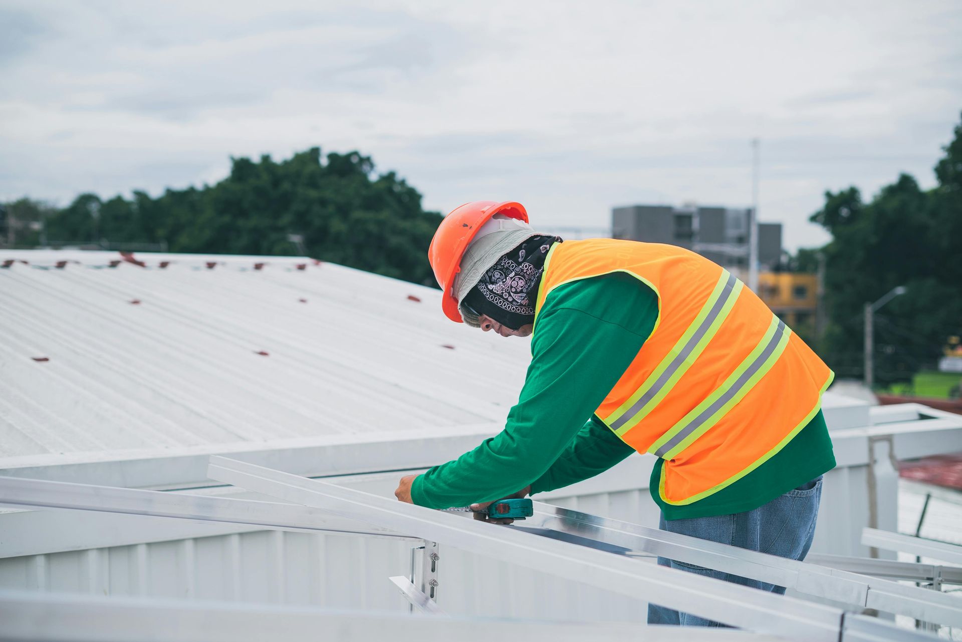 Construction worker on a roof wearing safety gear, working with metal beams under a cloudy sky.