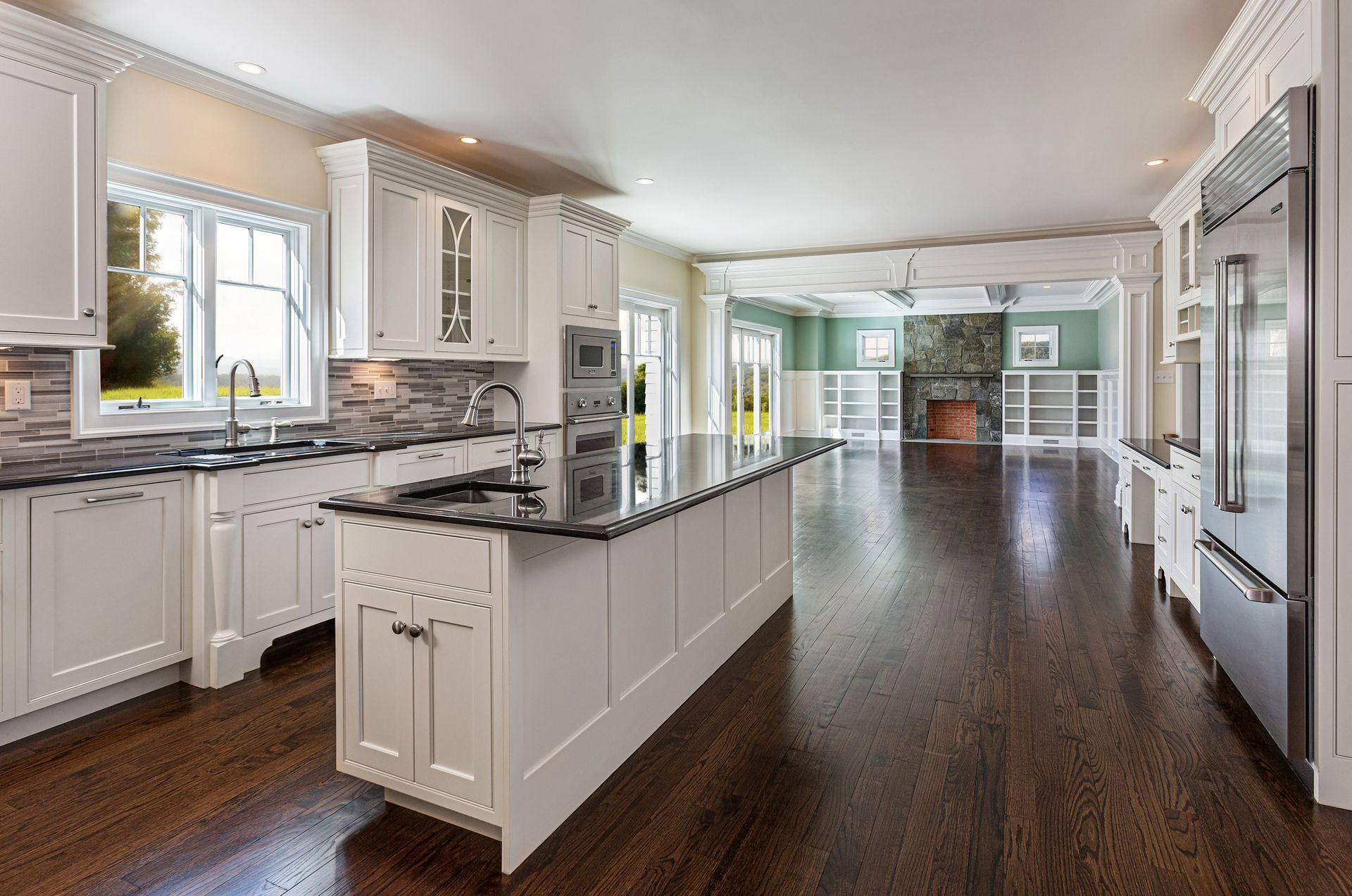 A kitchen with white cabinets, black counter tops, stainless steel appliances and hardwood floors.