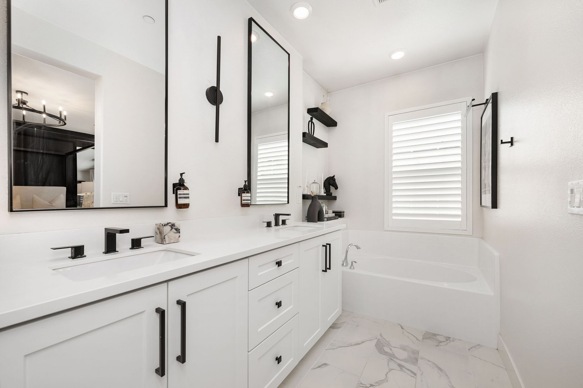 A bathroom with two sink, two mirrors, a tub and a window.