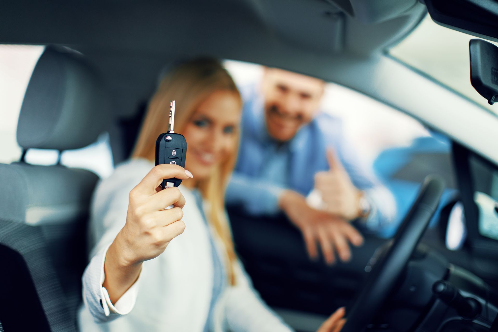 A woman is sitting in a car holding a car key.