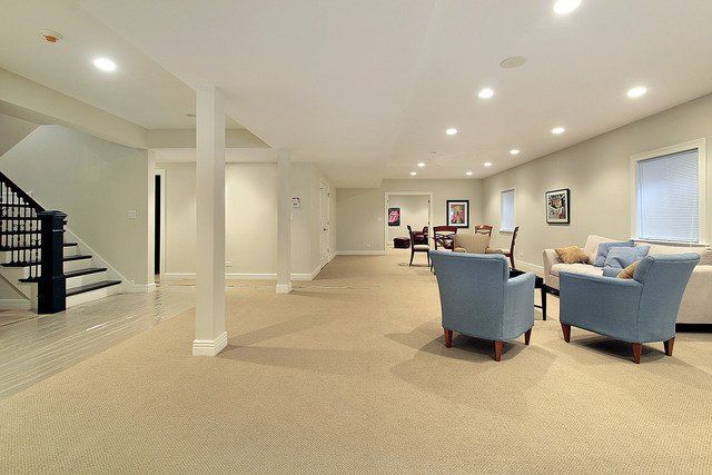 A living room in a basement with a staircase and chairs.