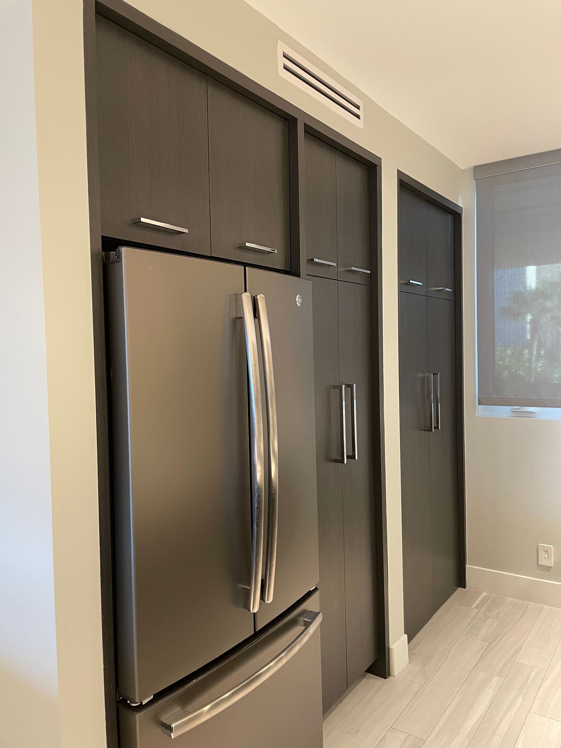 A black refrigerator is built into a wall in a kitchen.