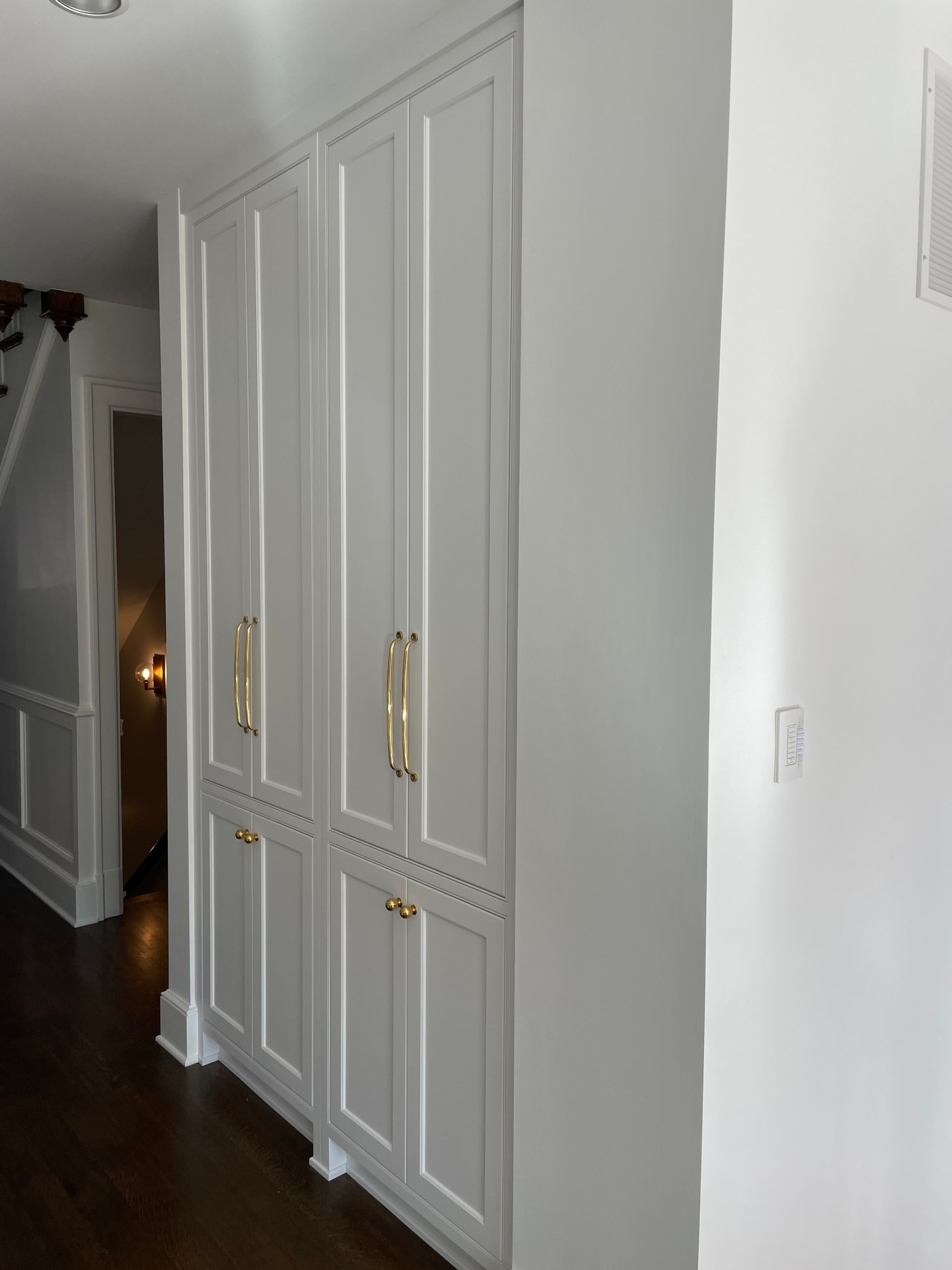 A large white cabinet with gold handles in a hallway.
