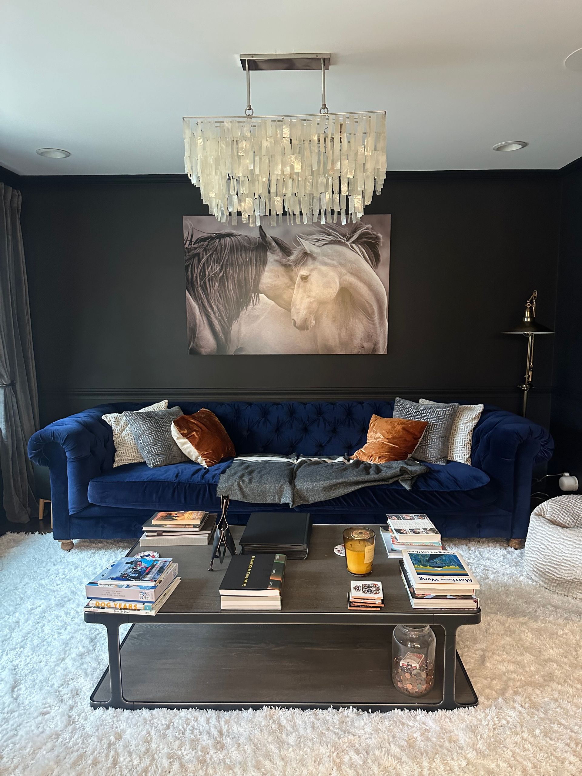 A living room with a blue couch , coffee table , and chandelier.
