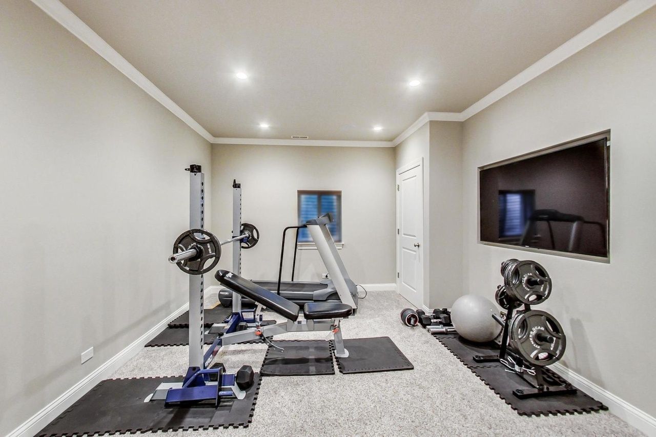 A basement gym with a treadmill , bench , dumbbells , and a television.